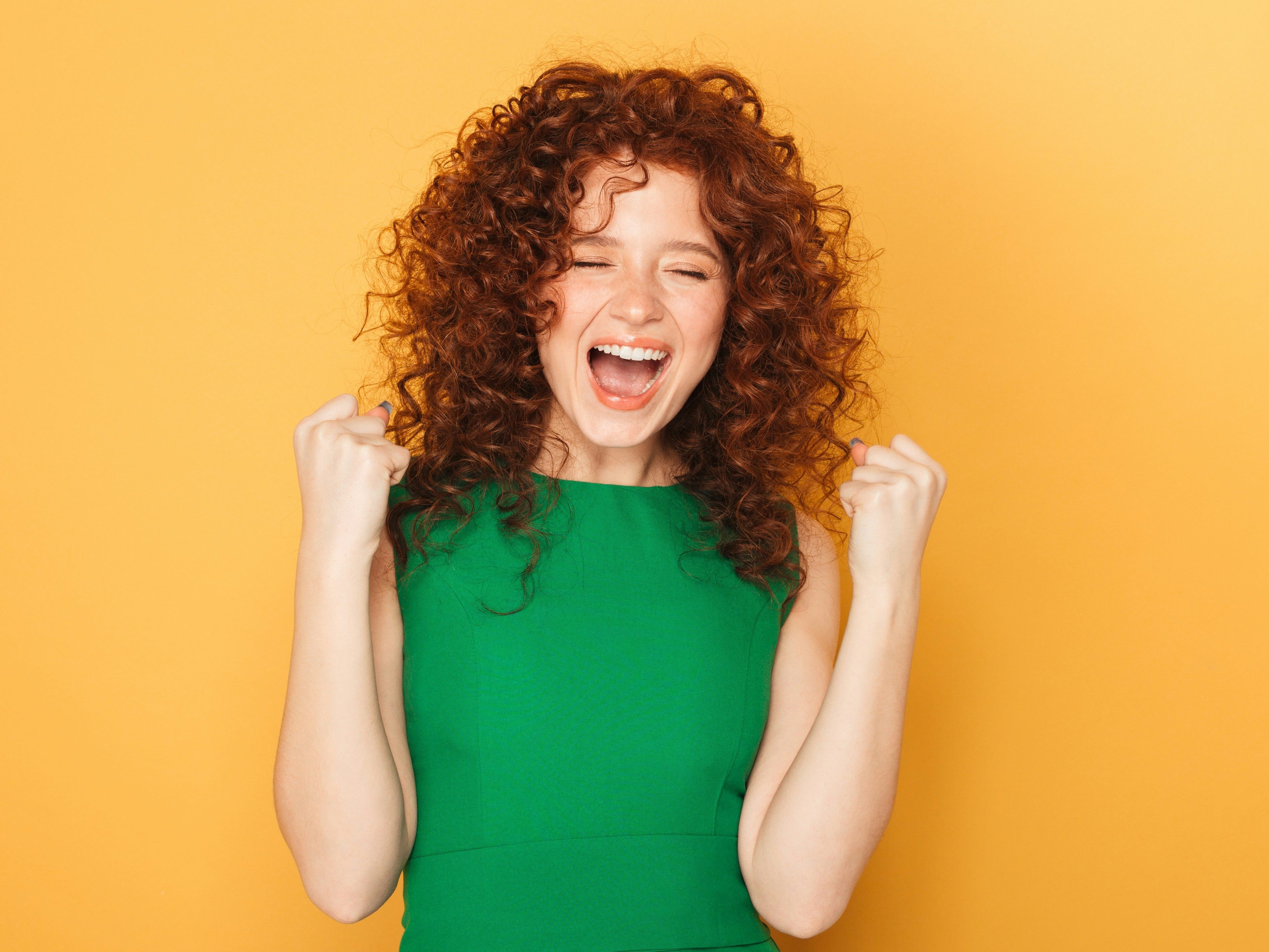 Woman wearing a green dress with a big smile and looking proud on a yellow backdrop
