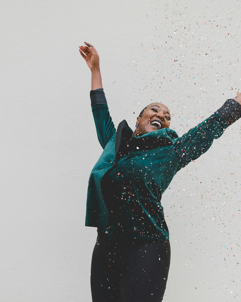 Photo of happy woman with her arms in the air and confetti falling. Photo by Clay Banks, unsplash