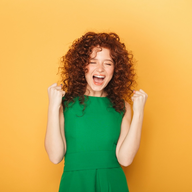 Woman wearing a green dress with a big smile and looking proud on a yellow backdrop